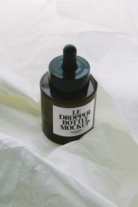 Dark amber dropper bottle mockup on pale yellow fabric backdrop