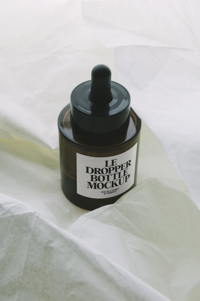 Dark amber dropper bottle mockup on pale yellow fabric backdrop