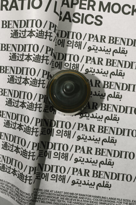 Rolled paper mockup with multilingual text on crumpled background, gold-rimmed black speaker on top