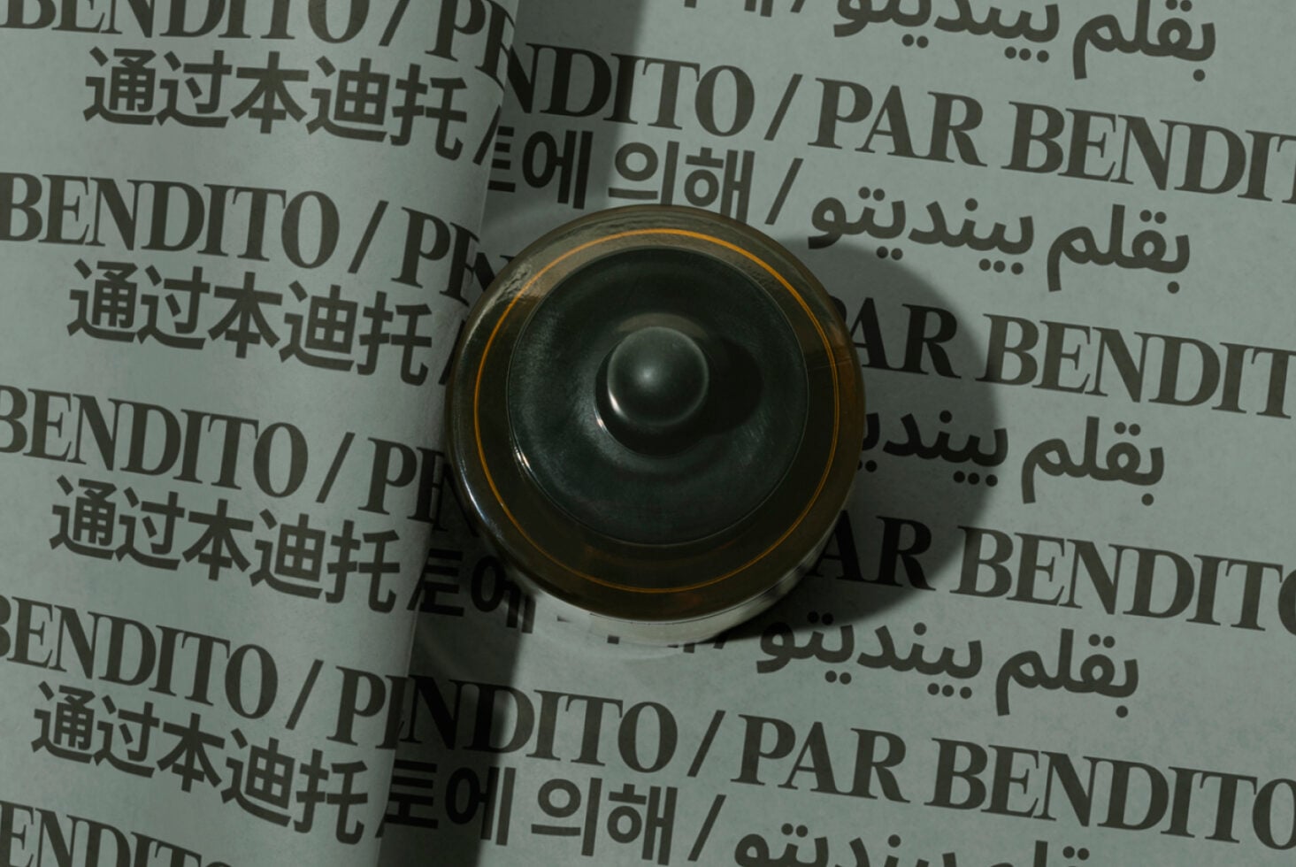 Overhead view of rolled paper mockup with multilingual text, gold-rimmed black speaker centered