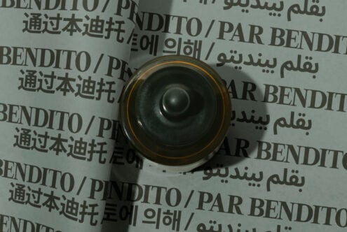 Overhead view of rolled paper mockup with multilingual text, gold-rimmed black speaker centered