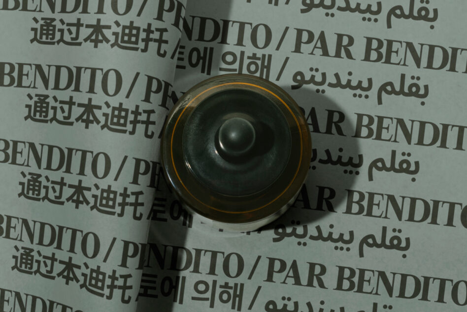 Overhead view of rolled paper mockup with multilingual text, gold-rimmed black speaker centered