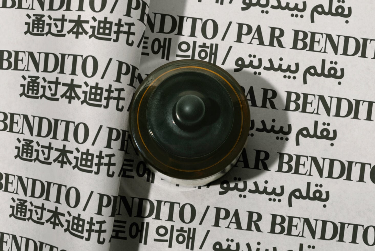 Overhead view of rolled paper mockup with multilingual text, gold-rimmed black speaker centered