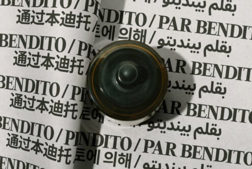 Overhead view of rolled paper mockup with multilingual text, gold-rimmed black speaker centered