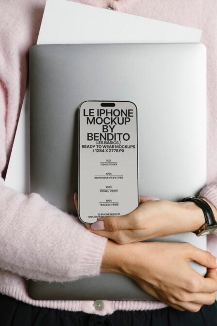 Person in pink sweater holding silver laptop with cream iPhone mockup