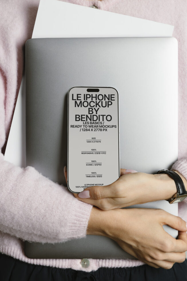 Person in pink sweater holding silver laptop with cream iPhone mockup