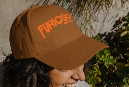 Side view of tan cap with orange Furioso text on person smiling outdoors near vines