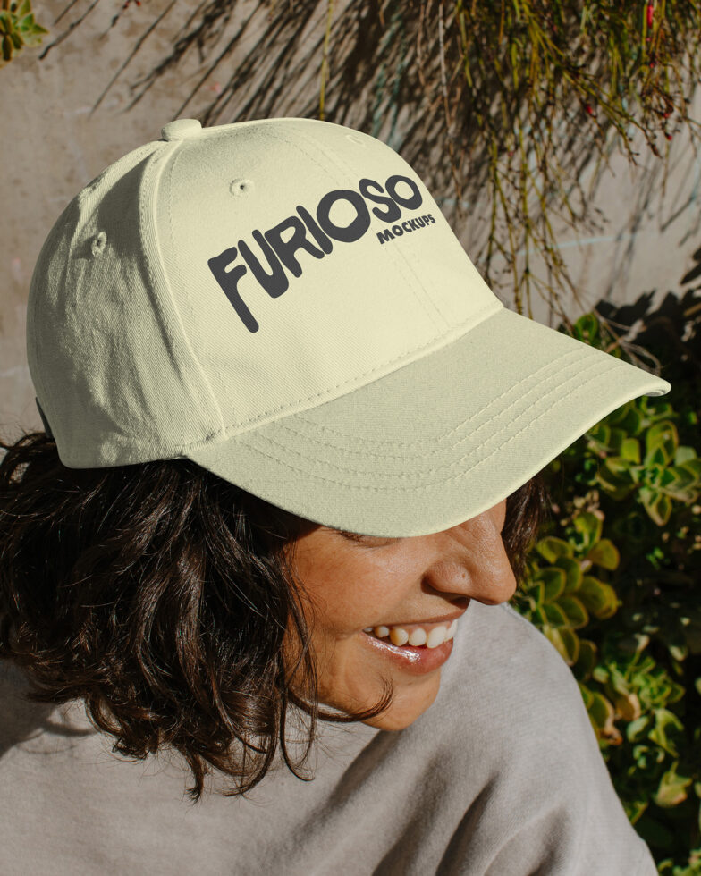 Woman wearing cream baseball cap with black Furioso text smiling in sunlight near plants