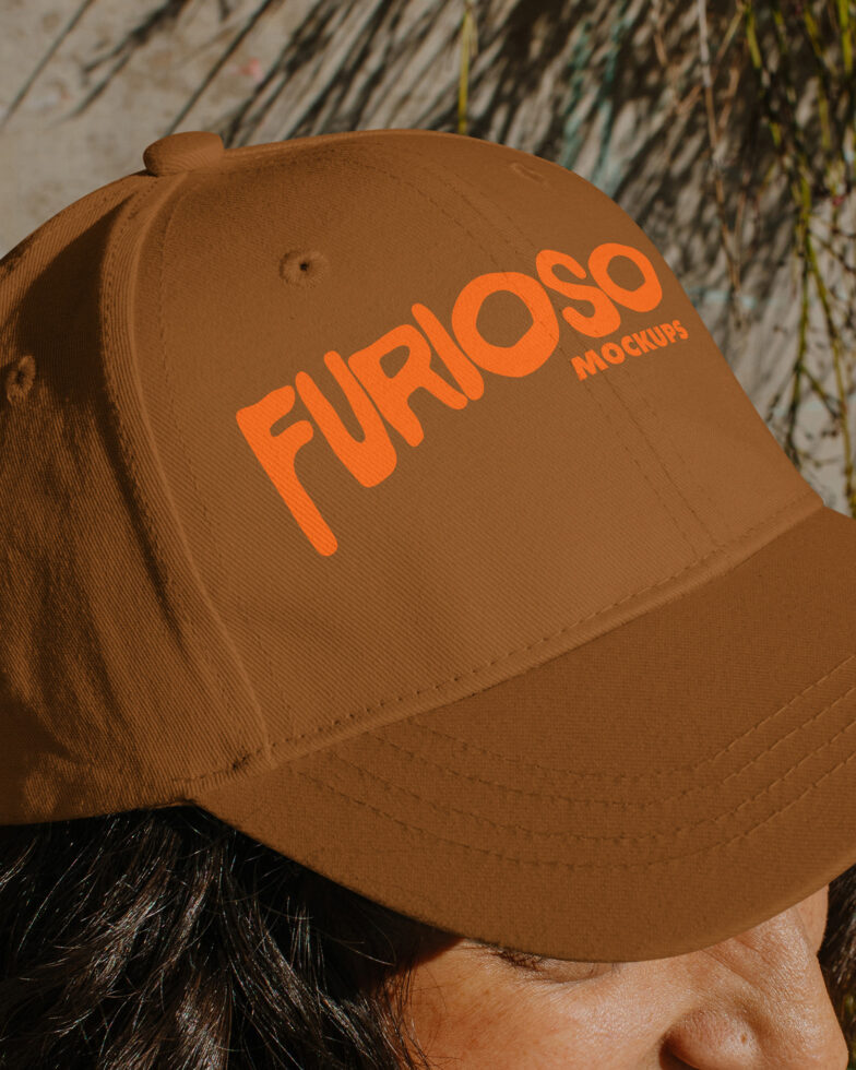 Close up of tan baseball cap with large orange Furioso text worn by person with dark curly hair