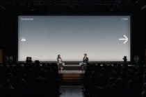 Auditorium projection screen with blue-gray gradient displaying white pixel arrow