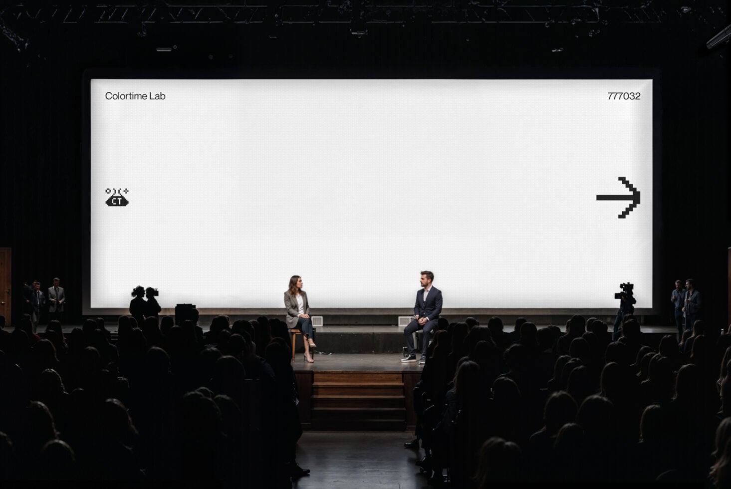 Large auditorium screen with bright white background showing black pixel arrow symbol