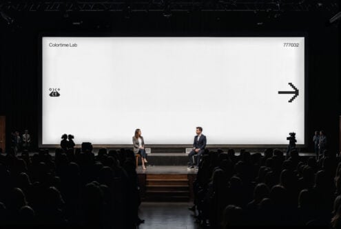 Large auditorium screen with bright white background showing black pixel arrow symbol