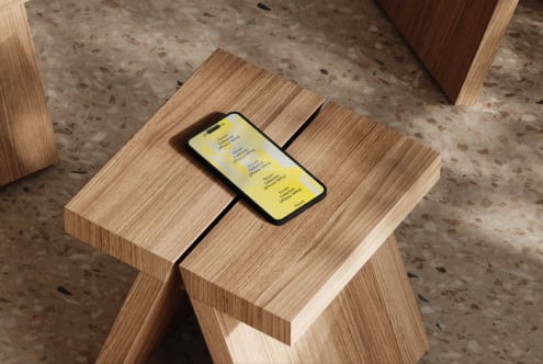 iPhone on wooden table showing yellow gradient screen in modern space