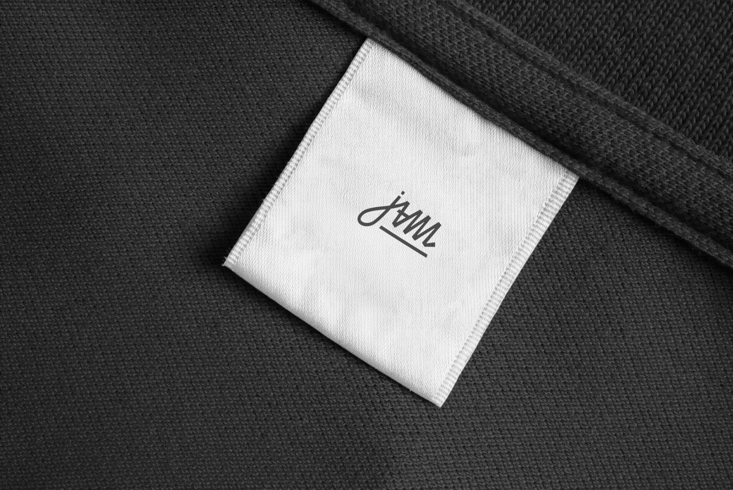 Black knit fabric with white care label displaying minimalist script signature