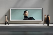 Wide horizontal frame on gallery wall showing portrait of woman in black turtleneck, visitors walking by