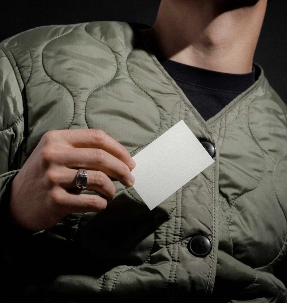 Person in quilted jacket holding blank white business card mockup