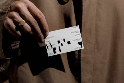 Hand holding white clothing label mockup against tan fabric background