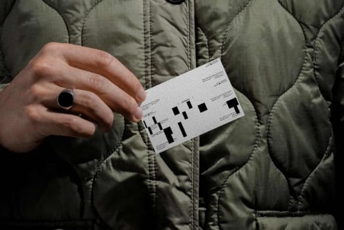 Person in quilted jacket holding white label mockup with same pixelated pattern