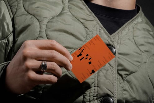 Person in beige quilted jacket holding bright orange business card mockup