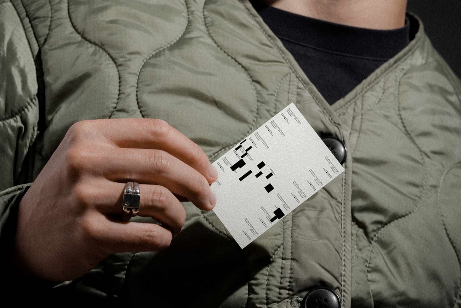 Hand holding white business card with black geometric pattern wearing quilted jacket