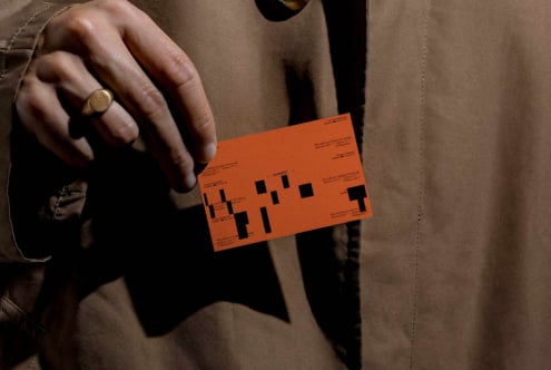 Orange business card with black geometric layout held in hand wearing gold ring