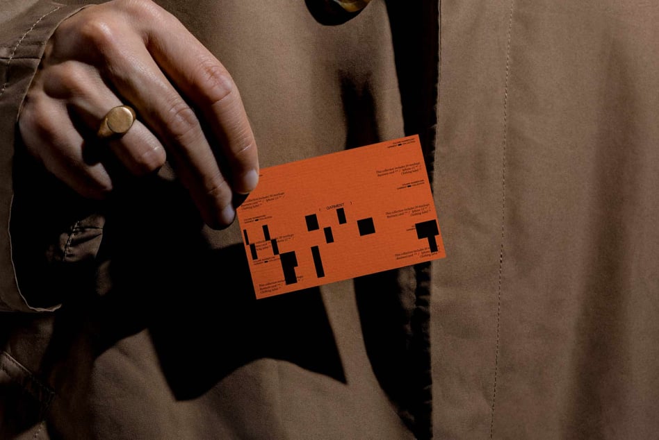 Orange business card with black geometric layout held in hand wearing gold ring