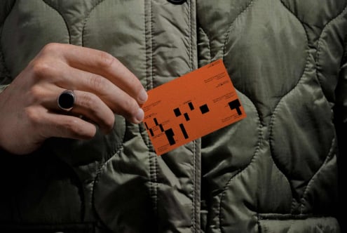 Person in quilted jacket holding orange label mockup with pixelated design