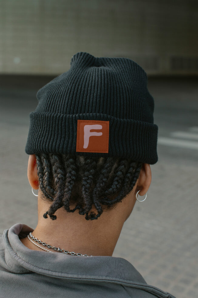 Dark knit beanie back view with burnt orange label patch displaying letter F
