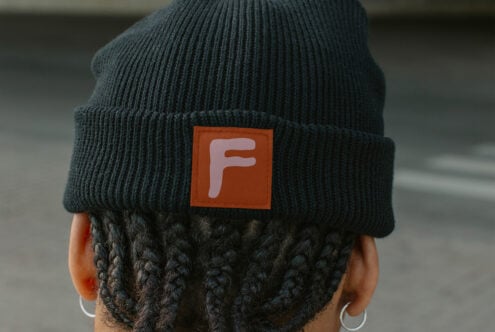 Dark teal beanie with small orange woven label patch showing F logo close up