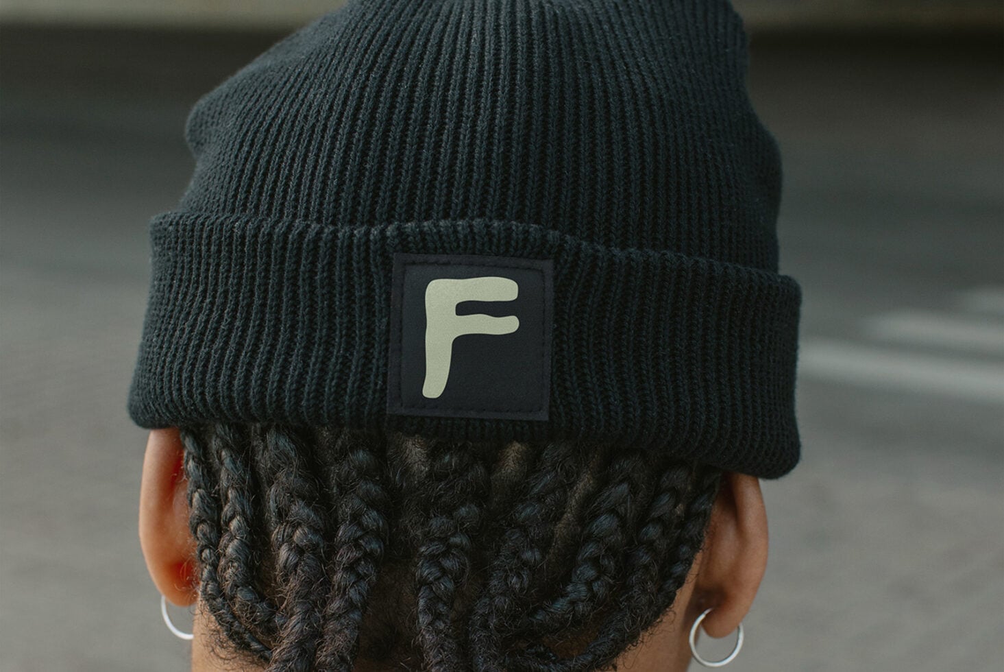 Back of head wearing dark beanie with cream colored square label patch with F initial