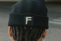 Back of head wearing dark beanie with cream colored square label patch with F initial
