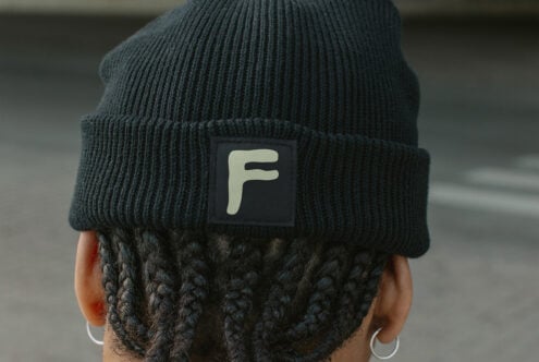 Back of head wearing dark beanie with cream colored square label patch with F initial