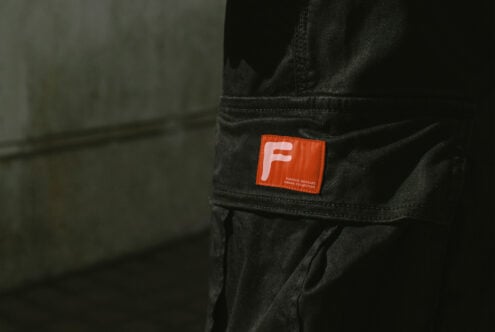 Orange woven label with F logo on black cargo pants leg detail
