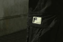 Cream label with F logo on black cargo pants pocket close up
