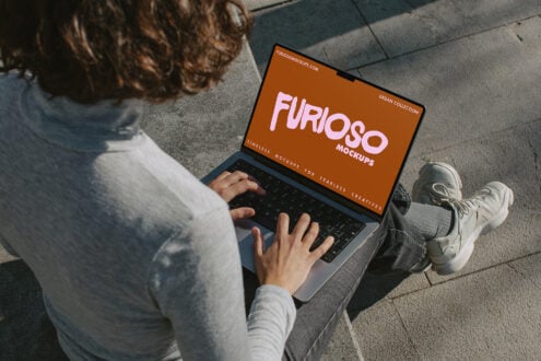 Designer working on laptop outdoors displaying Furioso Mockups orange banner
