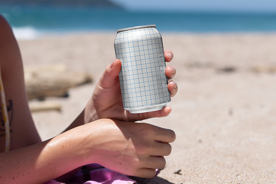 Close up slim can mockup with grid overlay held on sunny beach with waves behind