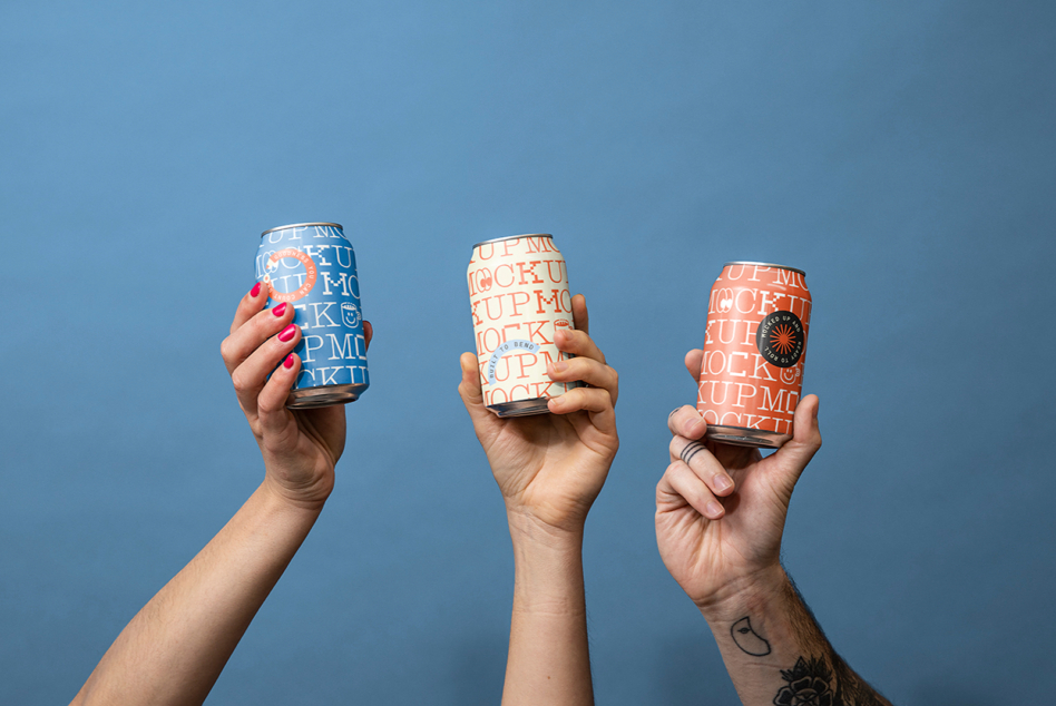 Three hands holding branded aluminum cans with text mockups against blue sky