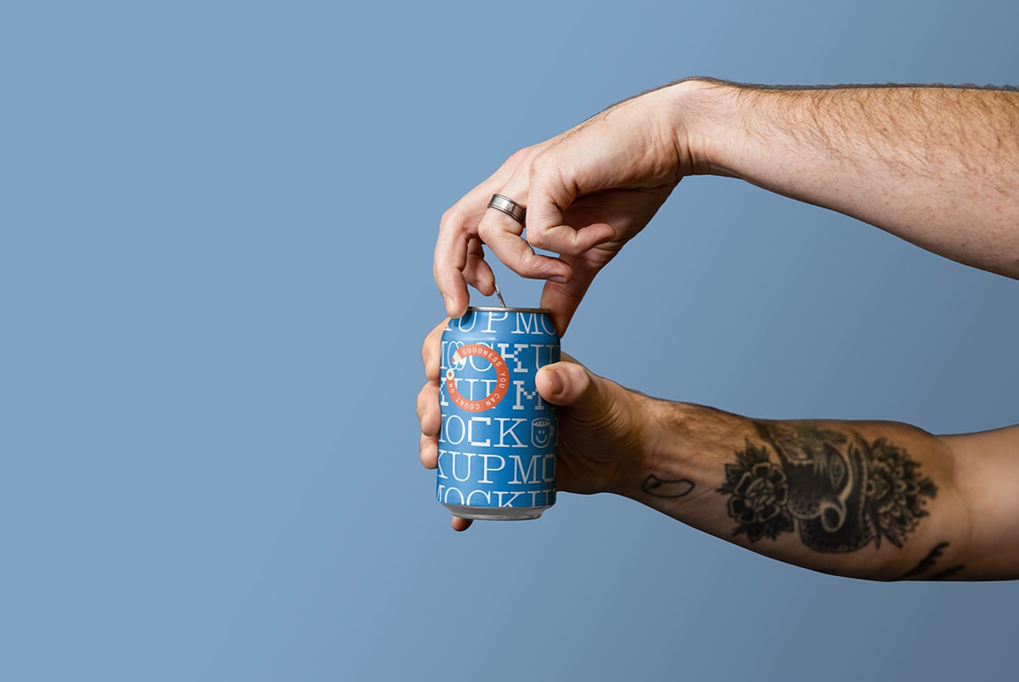 Tattooed hand holding blue beer can with orange badge against blue sky