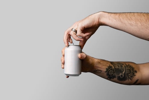 Tattooed hand holding blank white grid-pattern can against neutral background