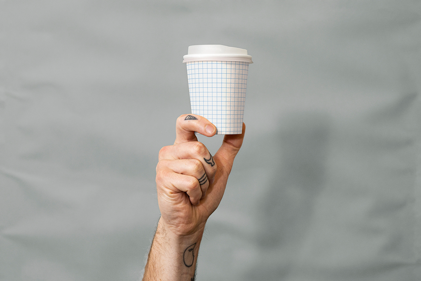 Hand holding blank coffee cup with grid overlay against cloudy background