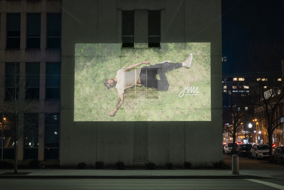 Overhead shot of person lying on grass displayed on urban billboard