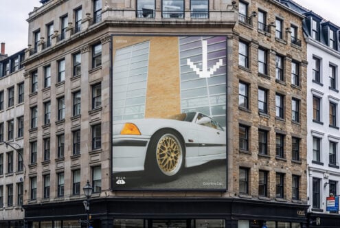 Large billboard showing white vintage car with gold wheels on pastel background