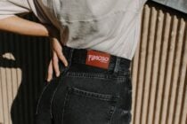 Rust orange fabric tag with pink Furioso text on jeans at hip level