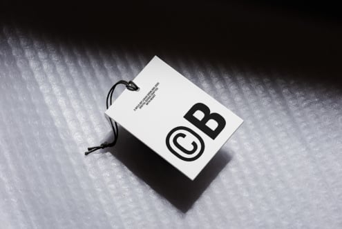 White hang tag mockup with black logo on textured concrete surface