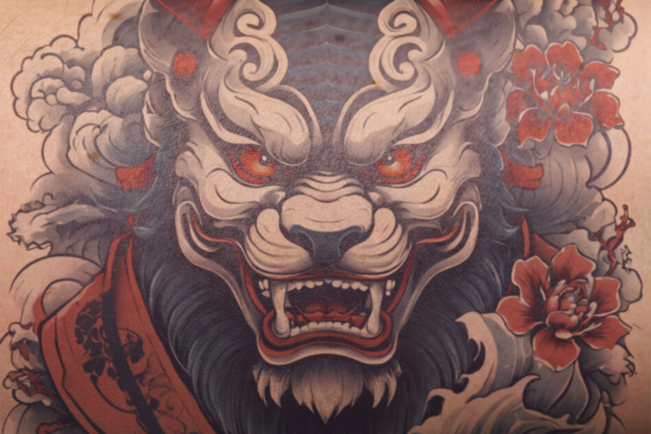 Ornate demon lion head tattoo with red eyes, flourishes, peonies