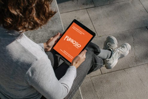 Overhead shot of person sitting on concrete holding tablet with orange screen displaying Furioso branding