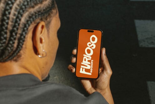 Person holding mobile device showing orange screen with white Furioso Mockups branding indoors