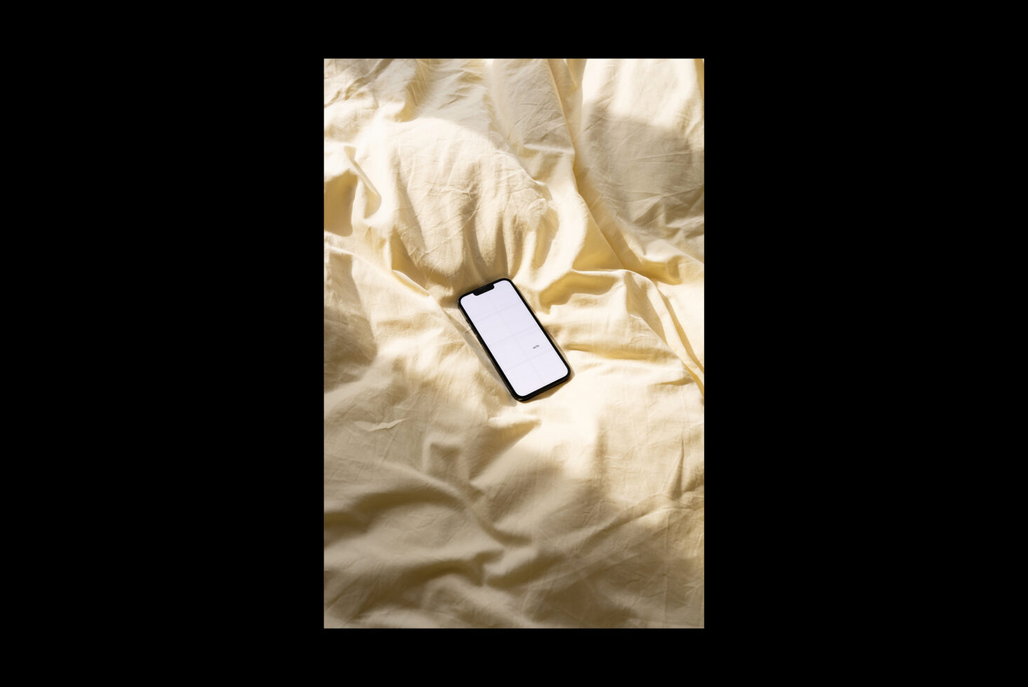 Black smartphone with blank screen resting on crumpled cream fabric