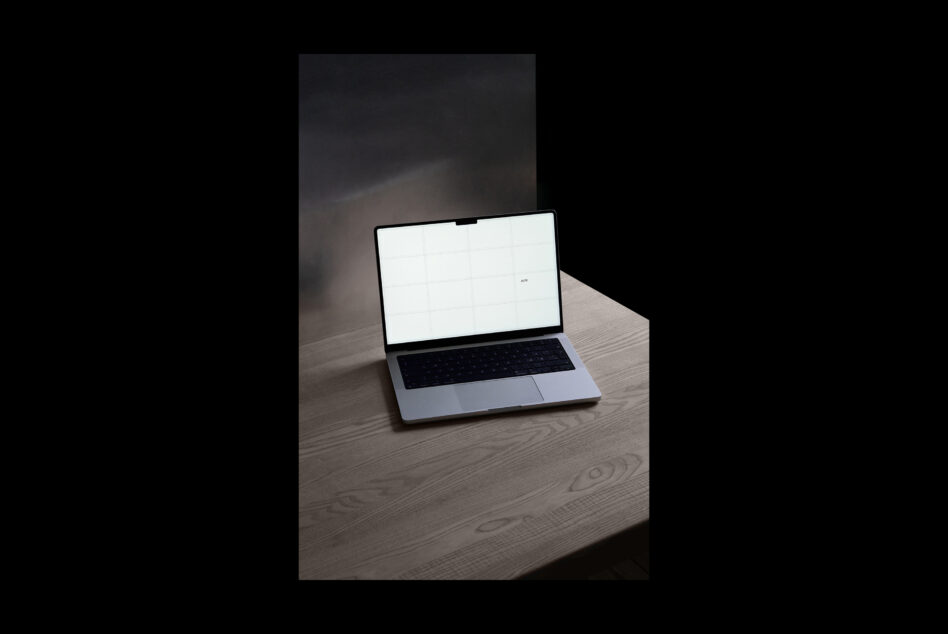 Silver laptop on wooden desk with blank screen, angled view against dark backdrop