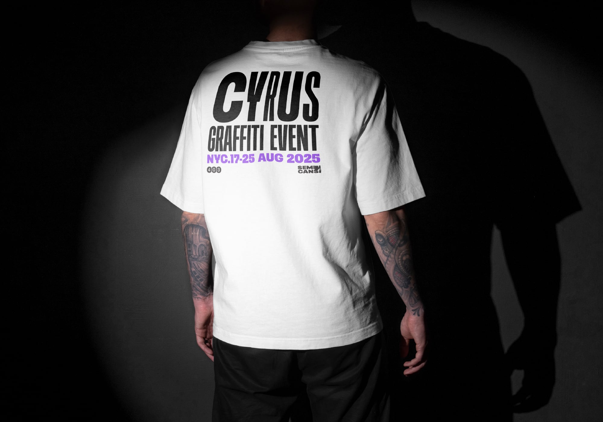 Back of white tee with CYRUS graffiti event text in black, tattooed arms visible